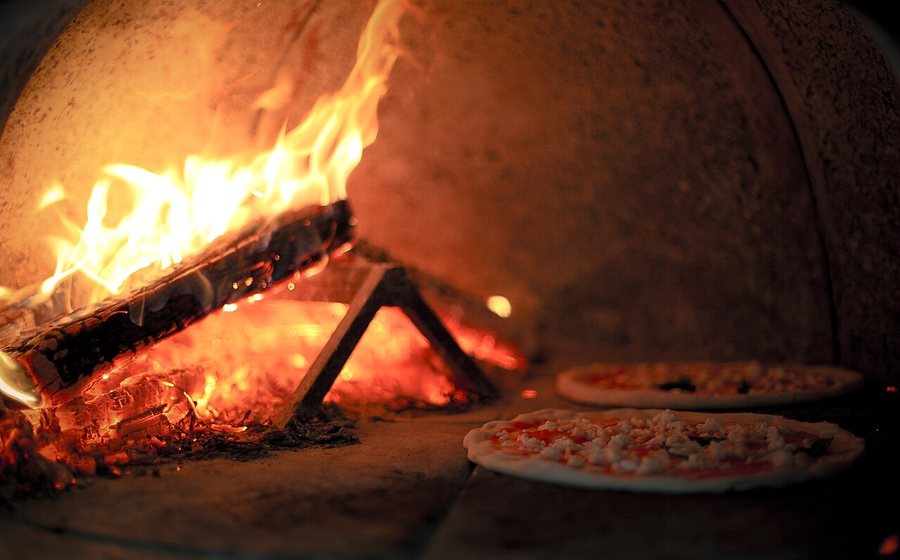 Pizzas baking beside a rolling wood fire inside a dome oven